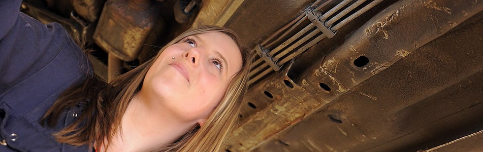 Female Motor Vehicle student under a car